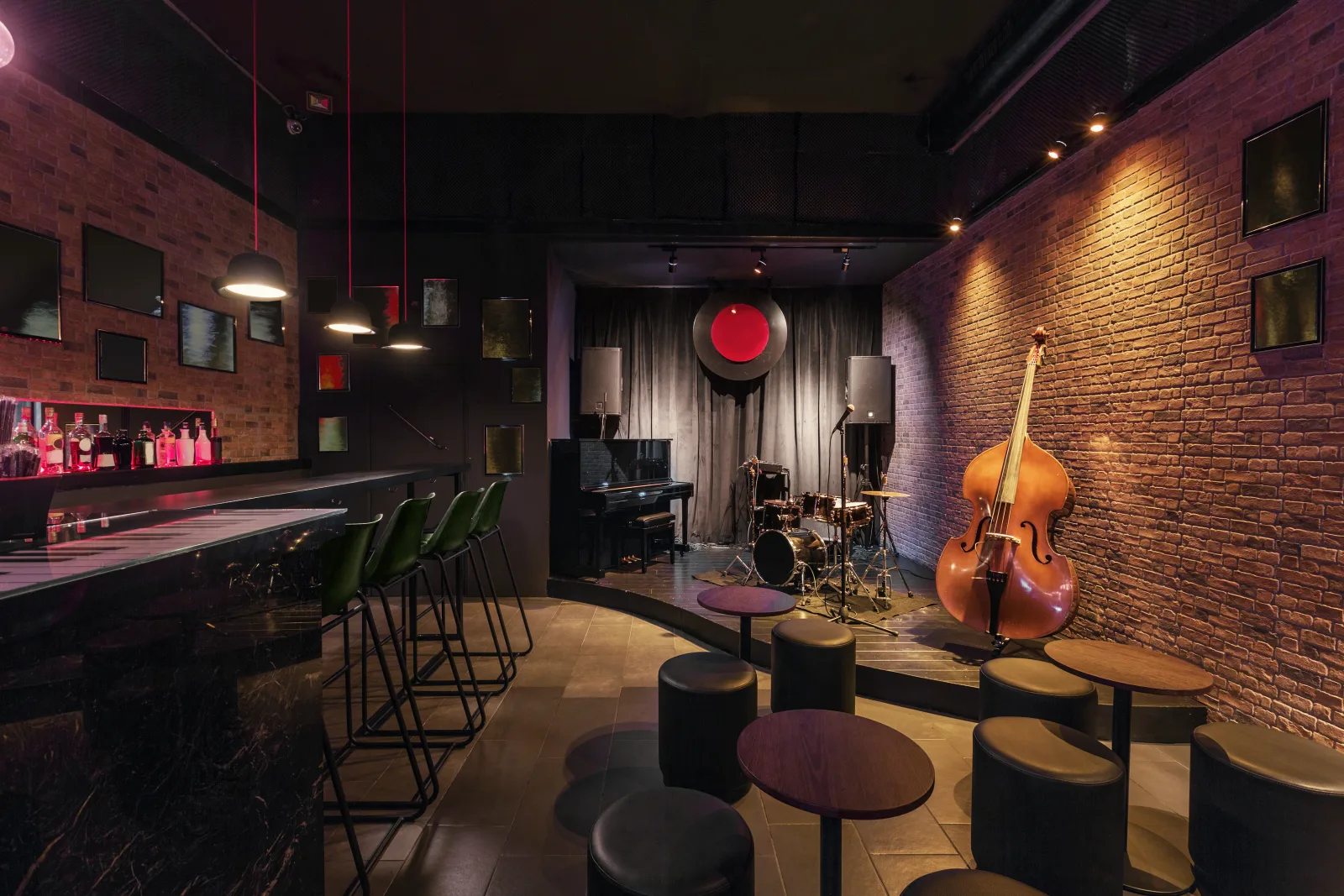 a dim bar room with a double bass, a drum kit and low stools against exposed brick — the coverage lines this brand writes