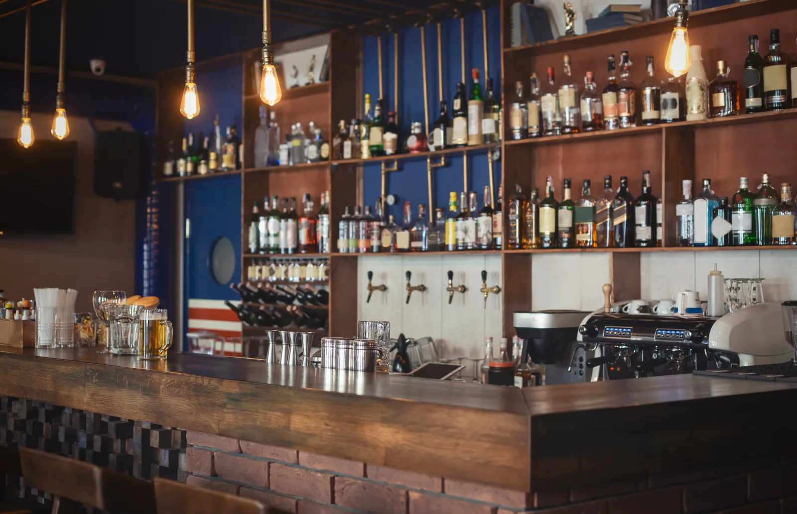 a bar counter with taps and a bottle-lined back wall under filament pendants — liquor liability and dram shop cover