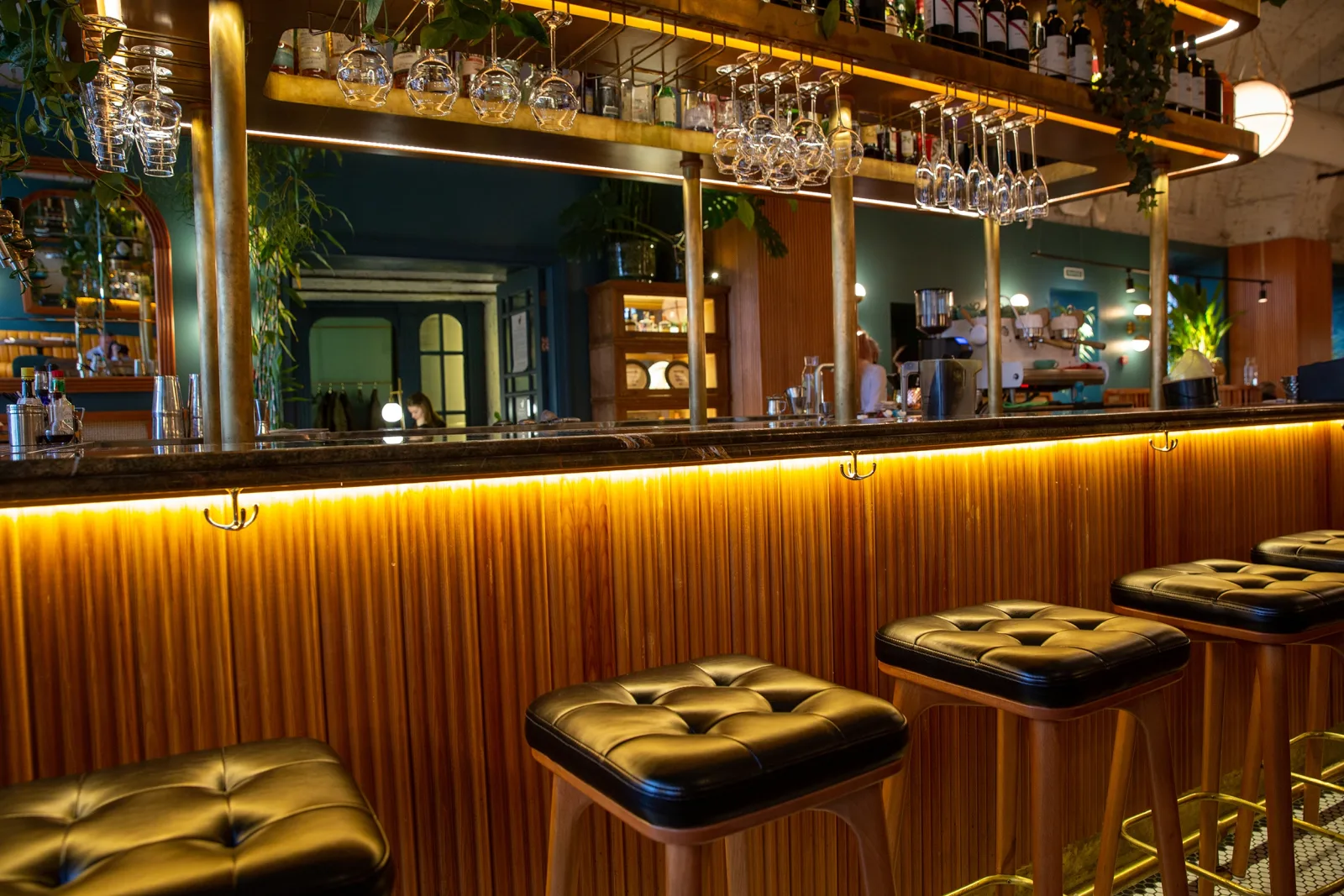 a curved bar with a brass rail, hanging stemware and buttoned leather stools — the states this brand is licensed in