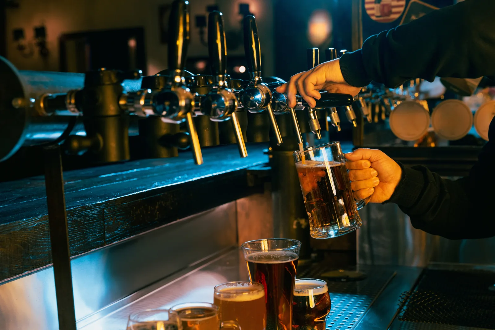 a hand pulling a pint from a row of taps under blue light — bar insurance in Delaware