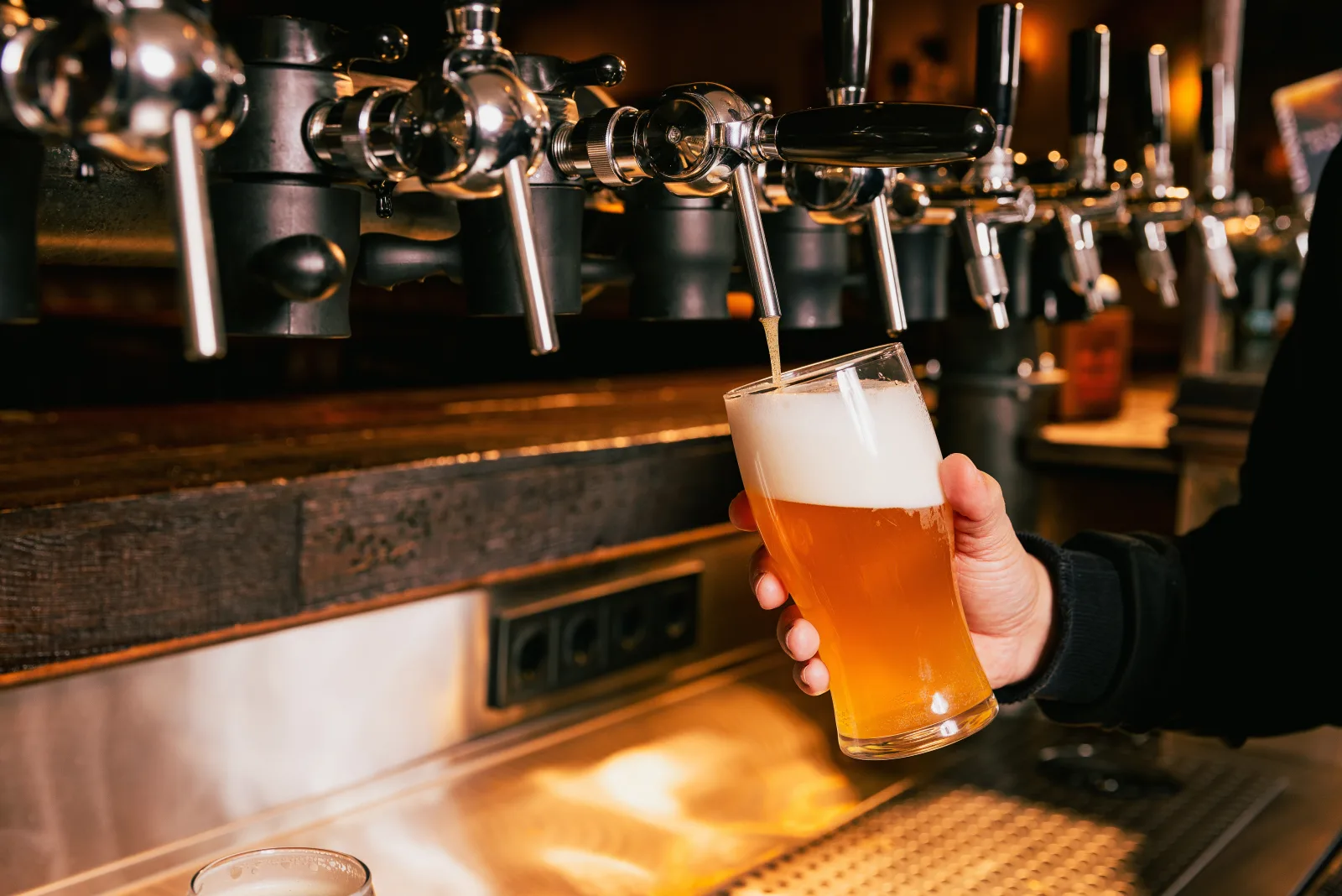 a hand holding a filled glass beneath a bank of chrome taps — bar insurance in Florida