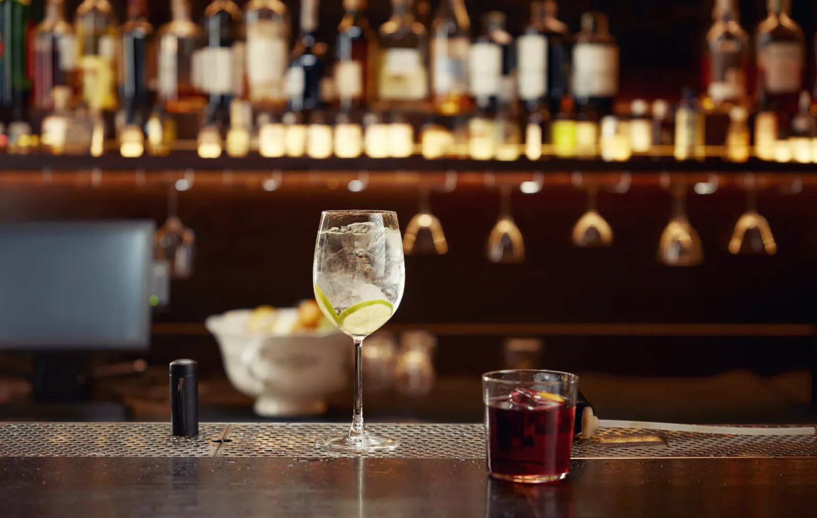 a wine glass and a dark drink on a counter in front of a lit spirits shelf — bar insurance in Texas