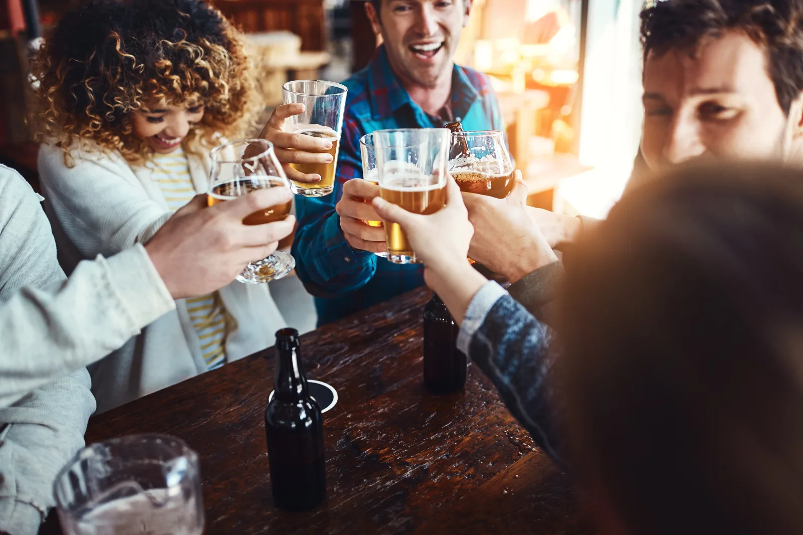three people raising glasses of beer at a wooden table — bar insurance in Utah