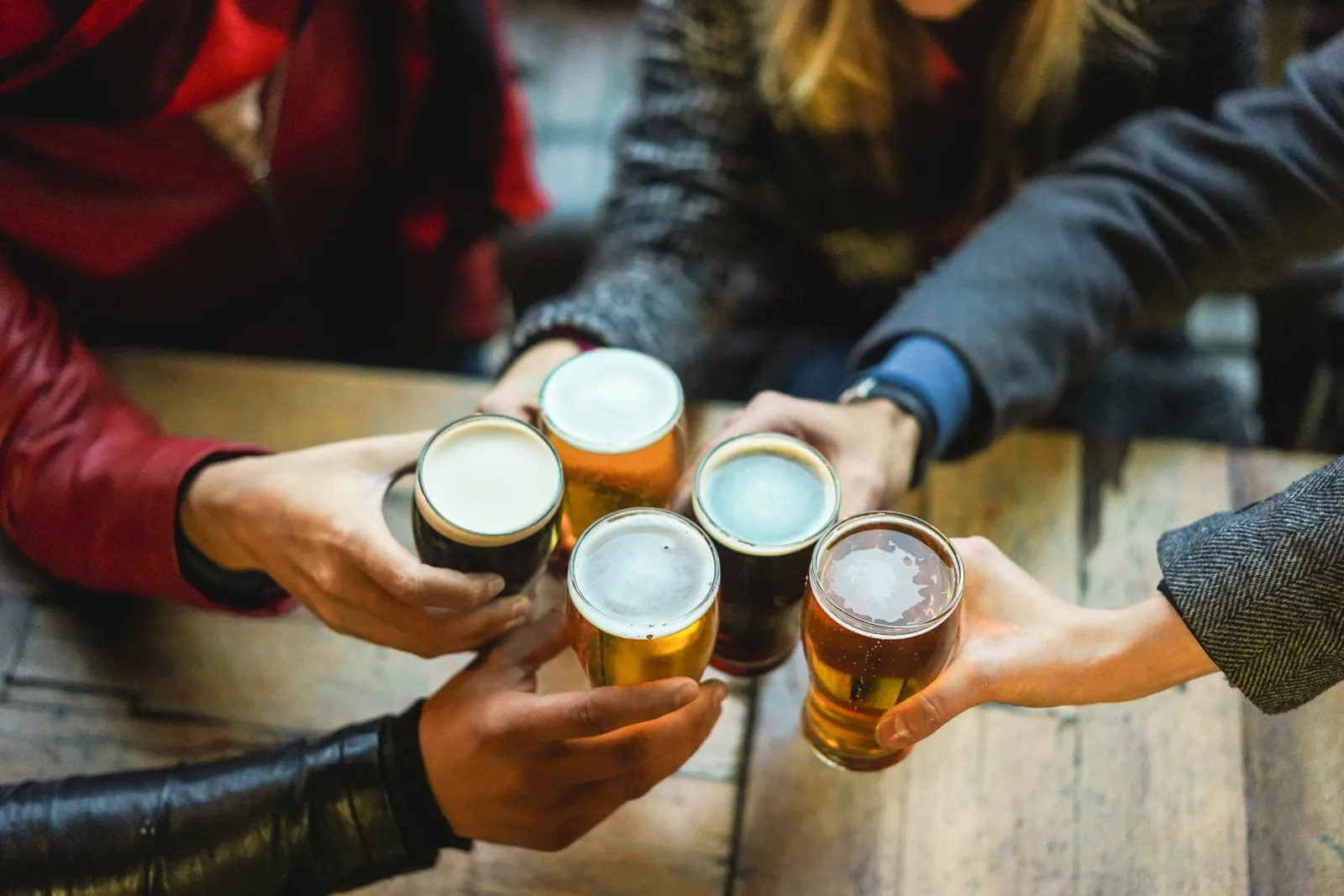 four hands bringing glasses of beer together over a table — bar insurance in Washington