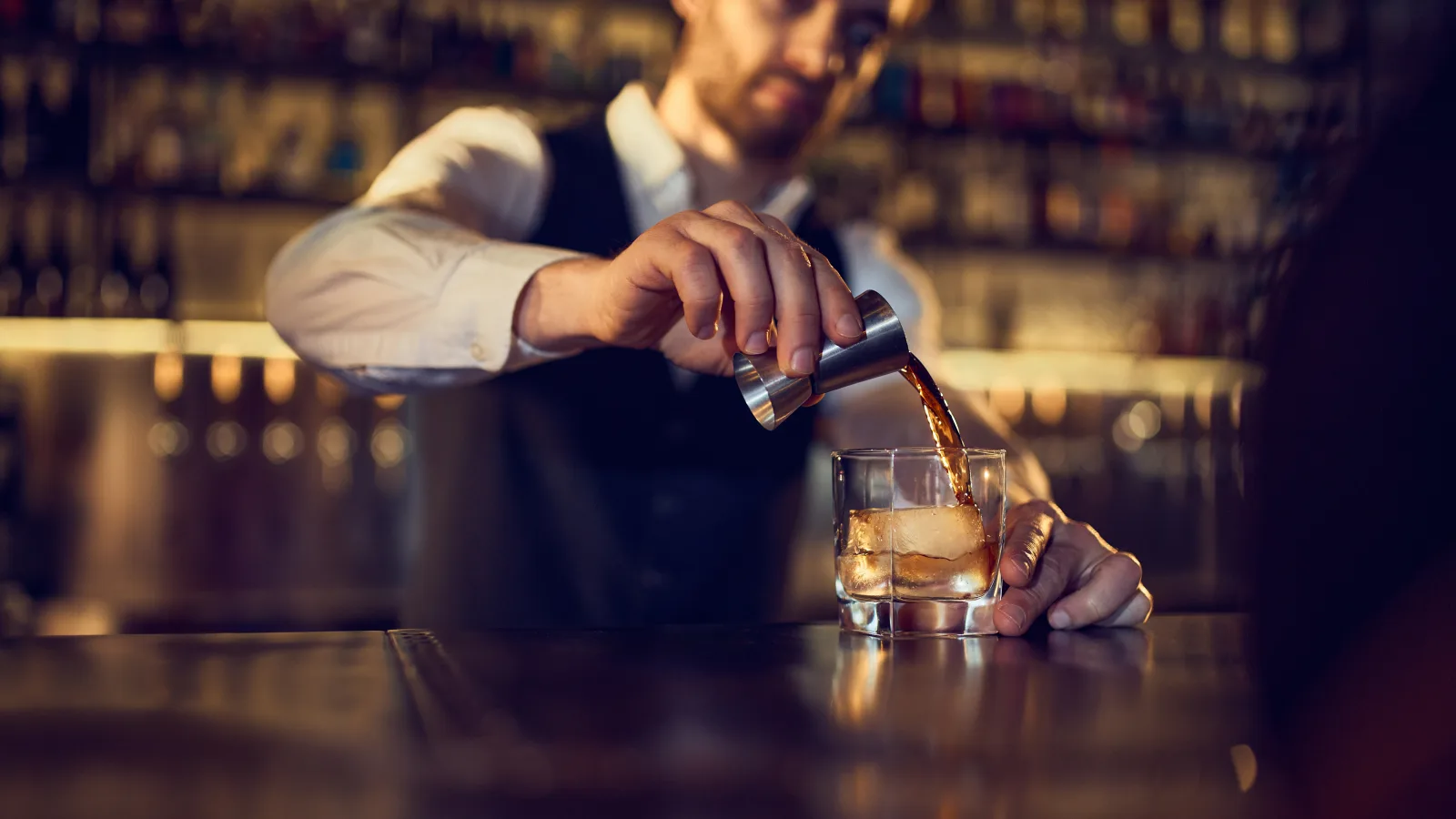 a bartender pouring from a shaker into a glass on a dark counter — bar insurance in Kansas