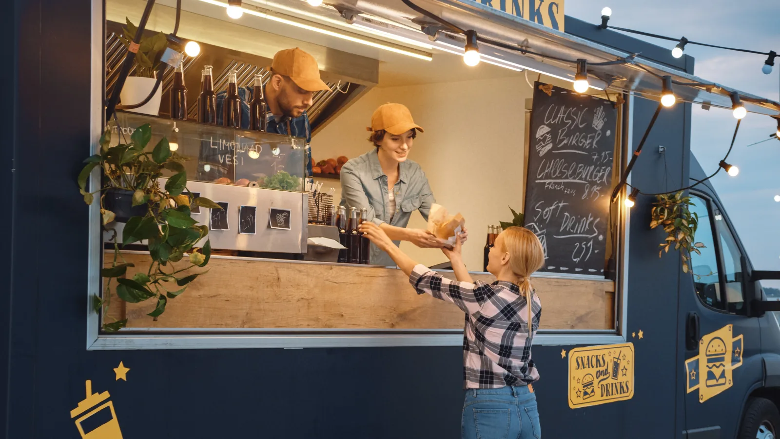 two staff in caps leaning through a service window to hand a wrapped order to a customer, a chalkboard menu and bottles behind them — spoilage and food contamination cover