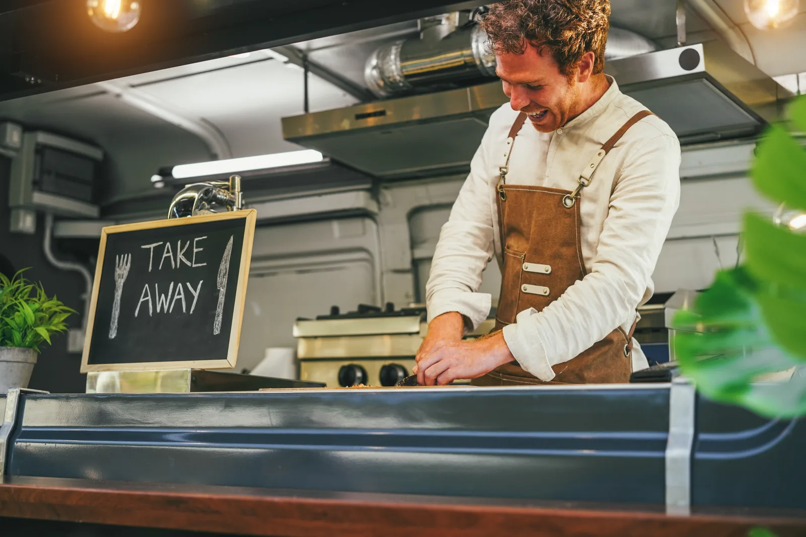 the inside of a food truck, a staff member in an apron working at a board beneath an extraction hood, a chalkboard propped on the pass — food truck insurance in Nevada