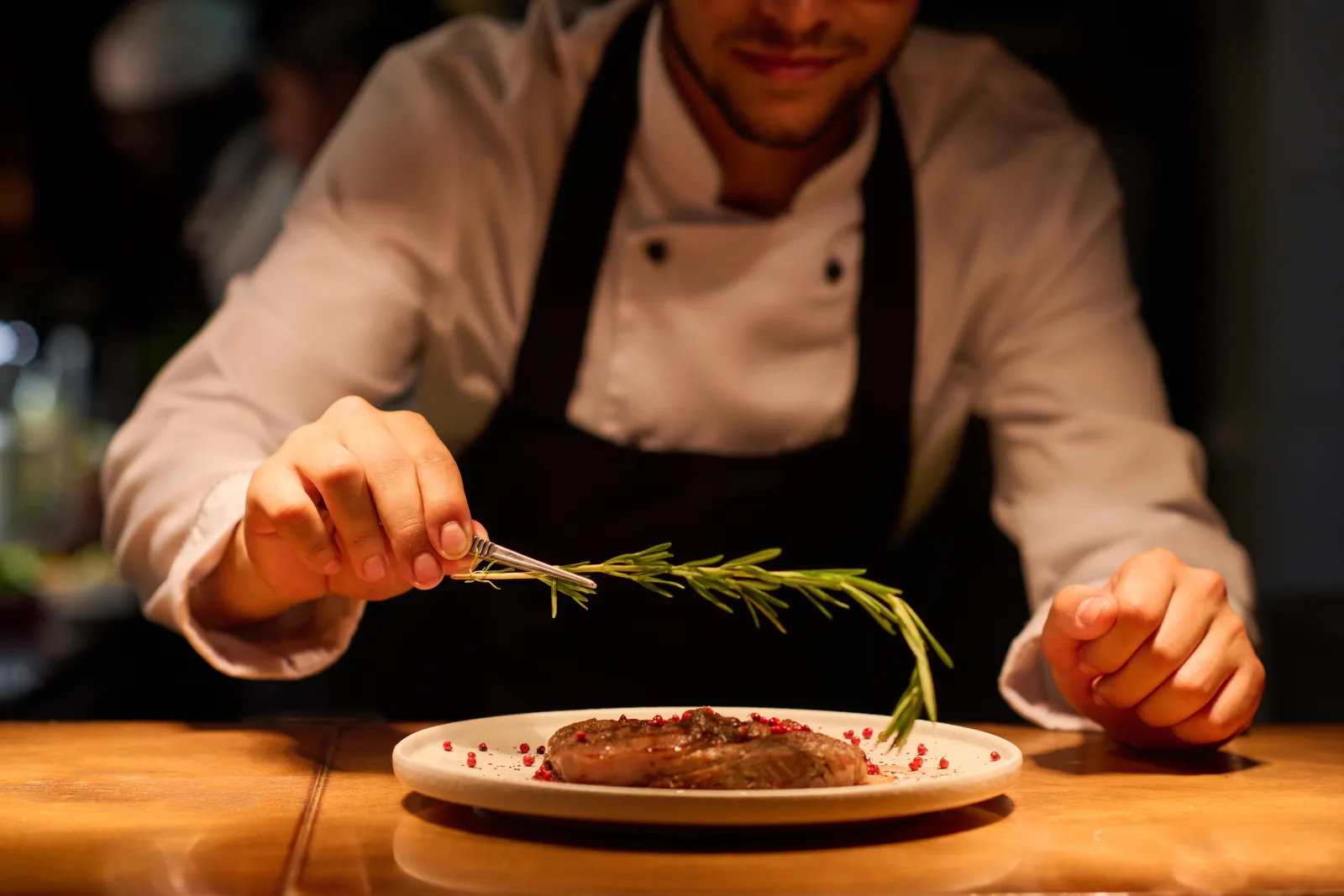 a chef in a white jacket and dark apron laying a sprig of rosemary onto a plated dish — commercial property for restaurants and bars