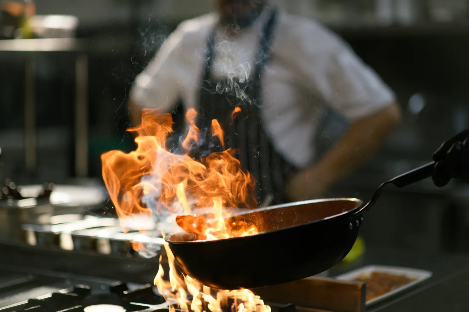 a cook tossing a flaming pan over a burner in a darkened kitchen — restaurant insurance in Texas