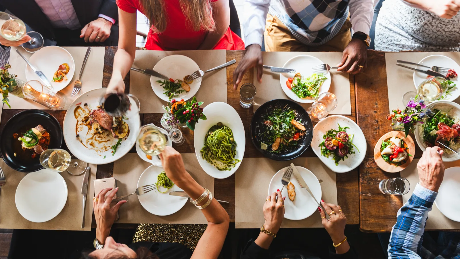 an overhead view of hands reaching across a table of shared plates — restaurant insurance in Florida