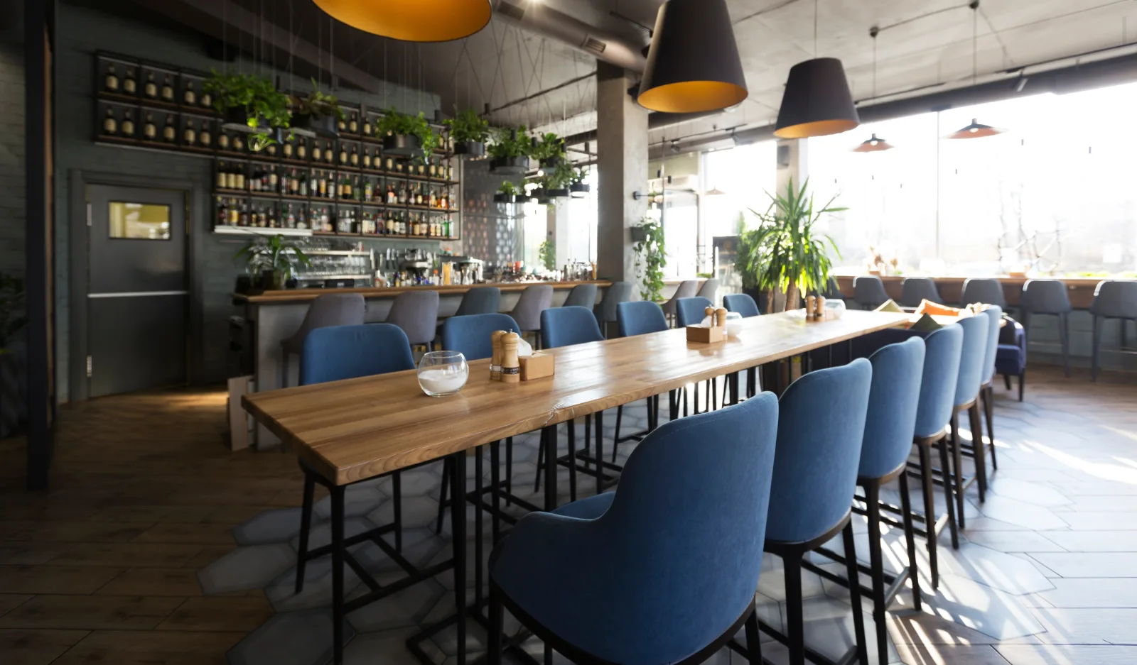 a long high table with blue chairs in front of a bottle-lined back bar — restaurant insurance in Indiana
