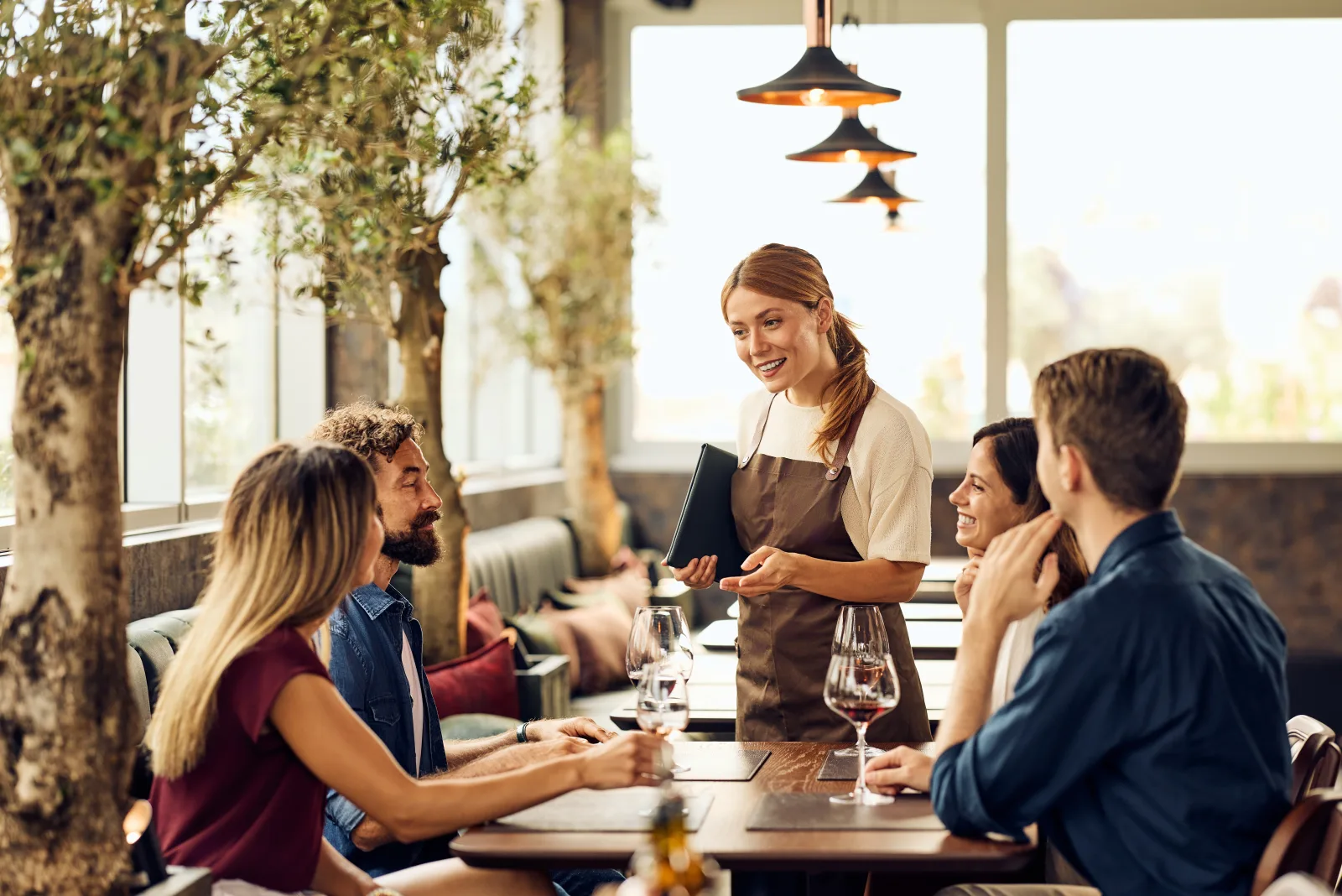 a server taking an order from four people seated under olive trees — restaurant insurance in New York